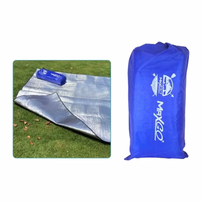Alfombra térmica MaxGo de aluminio doble cara extendida sobre el pasto con su bolsa azul encima